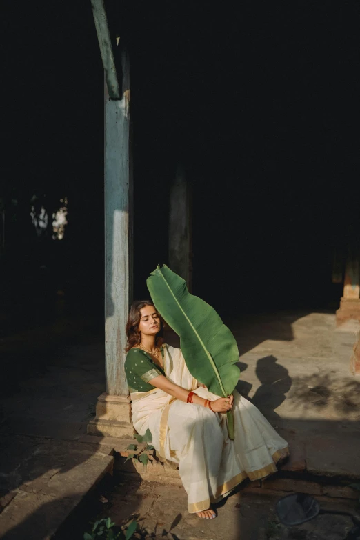 a girl is sitting on a concrete step holding a large green leaf