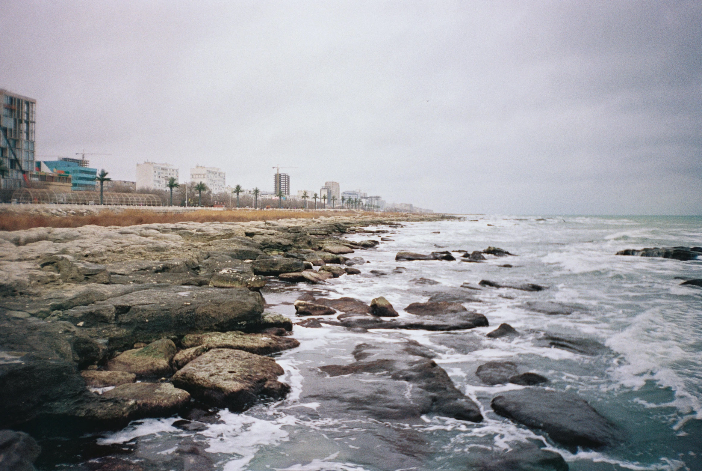 the ocean and rocks is next to an oceanfront with buildings