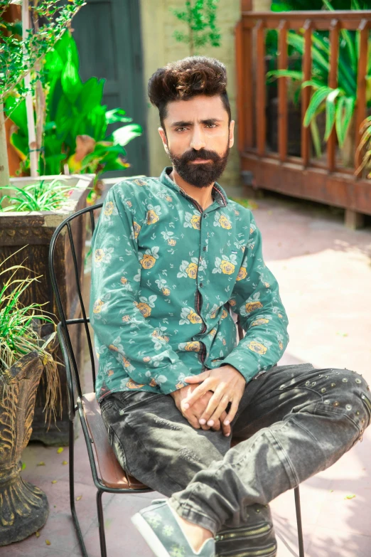 a man sitting on a chair with a beard and wearing a green shirt