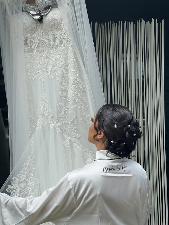 a woman in a white jacket looking at a wedding dress