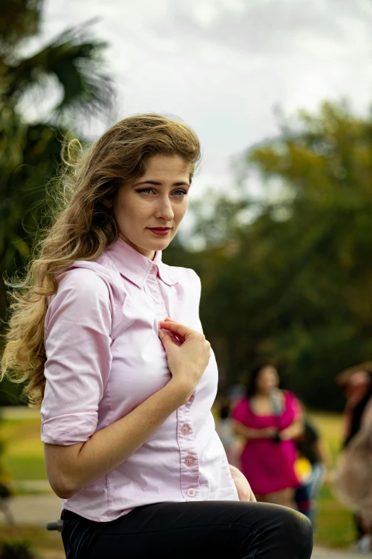 a beautiful woman wearing a pink blouse standing near a lake