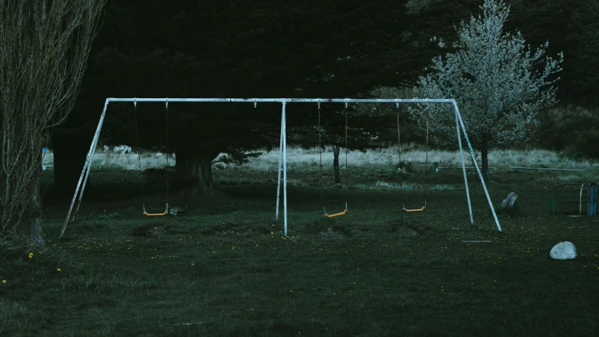 an empty, metal swing set on the ground in the dark