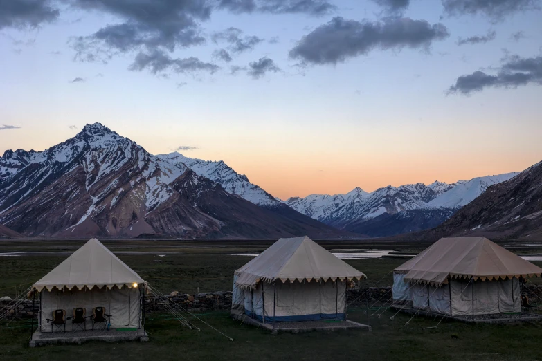 a group of three tents in a field near mountains