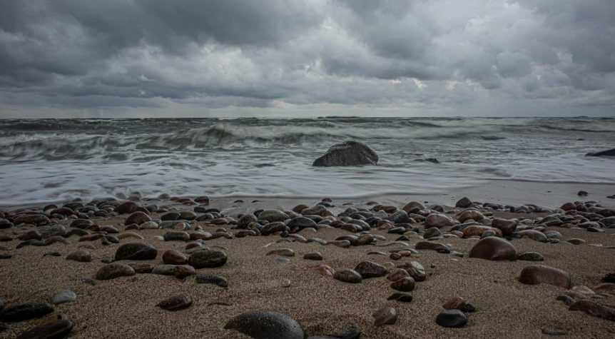 many rocks in the sand and a large wave crashing against the beach