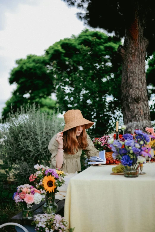 the woman is sitting at a table with flowers and a hat