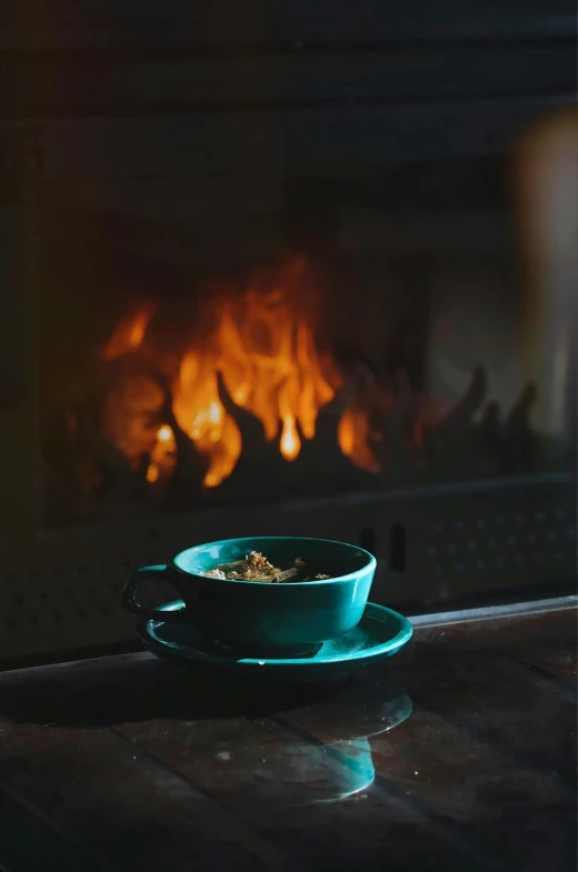 teacup sitting on plate by fireplace lit in dark room