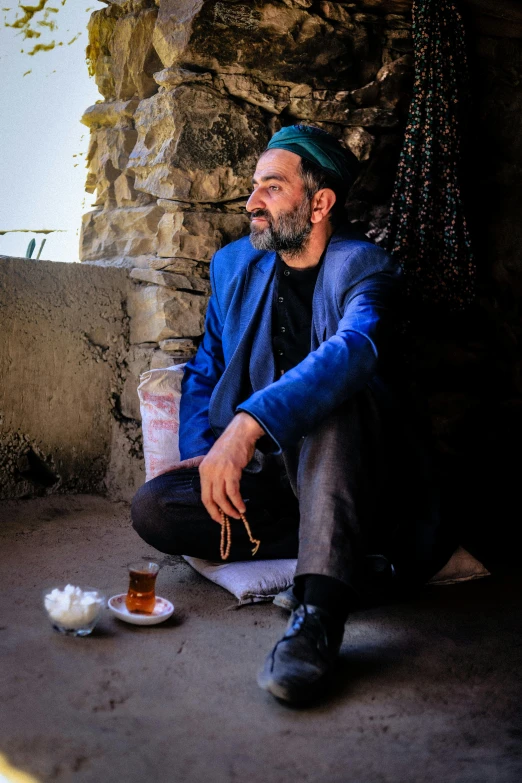 a man with a drink sits against a wall in front of a wall