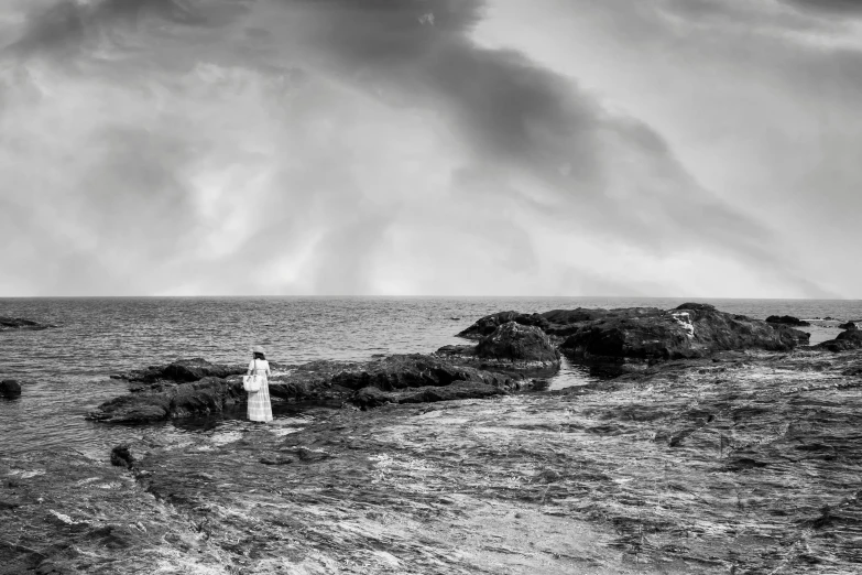 black and white pograph of two people in a field, in front of a rocky coast