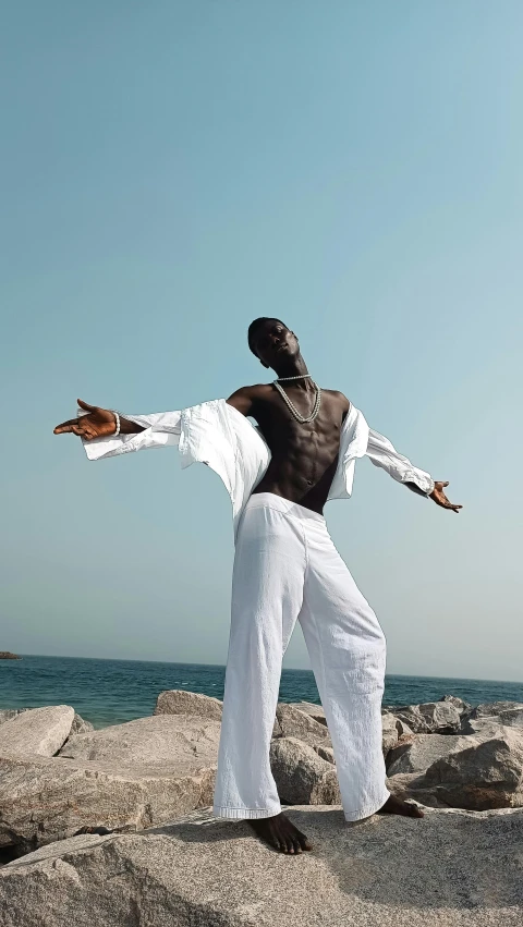 a man in white pants dancing near the ocean