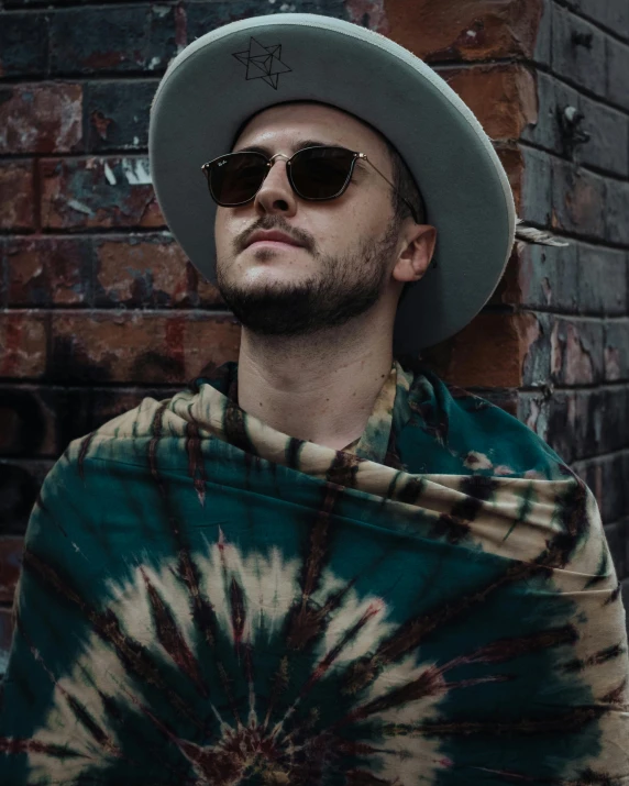 man with a tie - dyed cape and hat looks into the distance