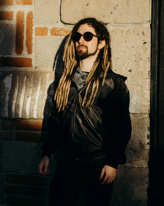 a man with long hair standing near a wall