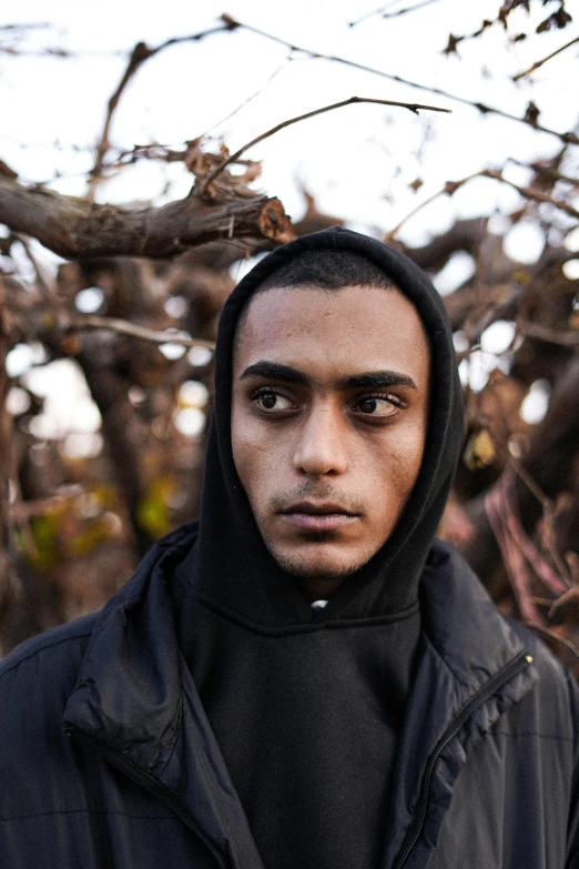 a man with a black hooded jacket is staring into the camera