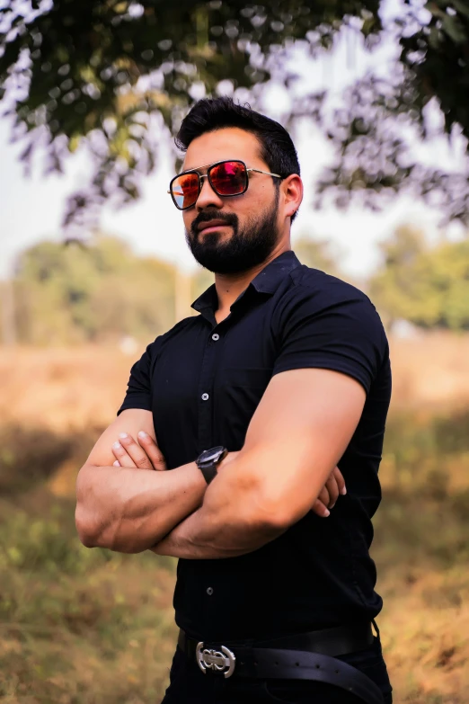 a man wearing sunglasses standing by a tree