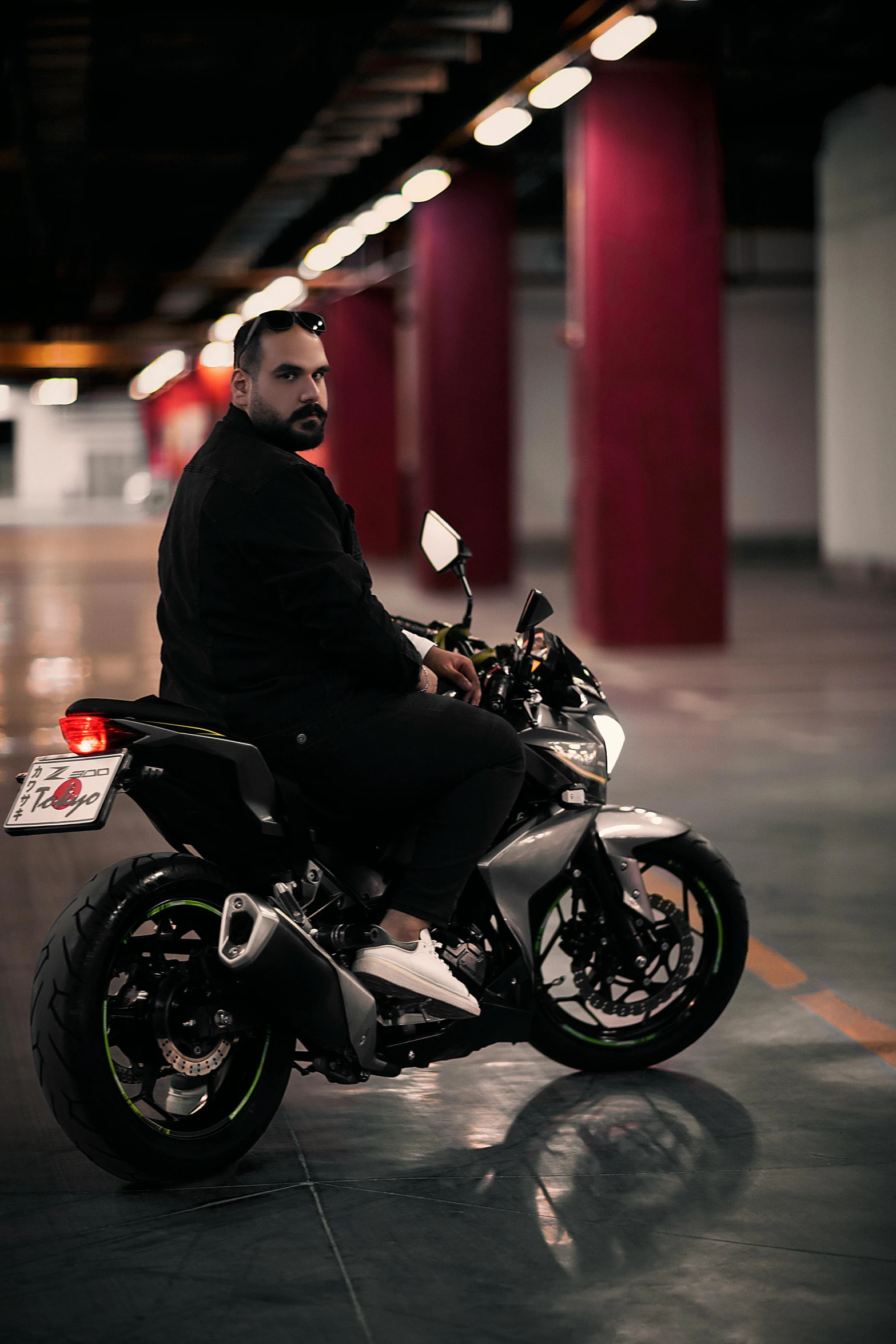 a bearded man sits on his motorcycle in an empty parking garage