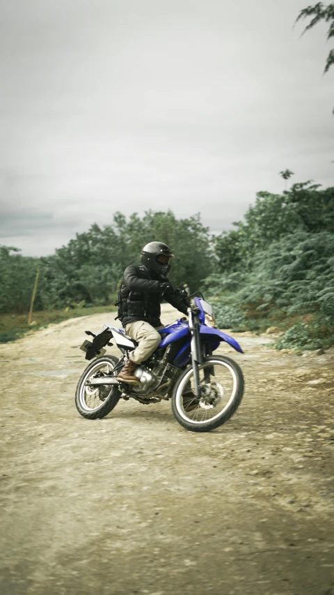 man in black jacket on blue motorcycle riding on gravel road