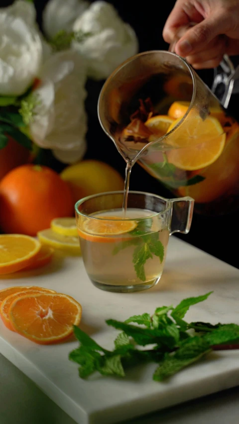 a person pouring a drink into a bowl filled with orange slices