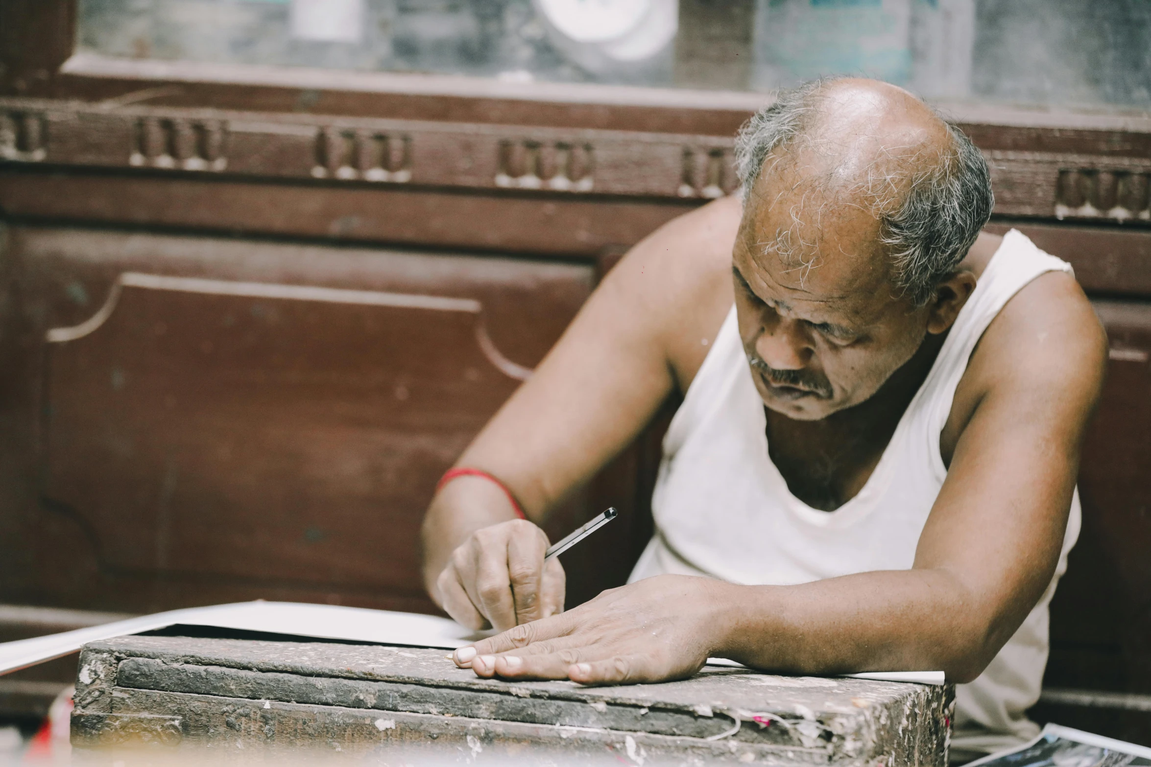 a man in a white tank top writes soing at a table