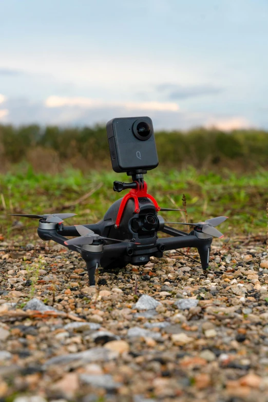 a small black and red remote controlled flying device on gravel ground