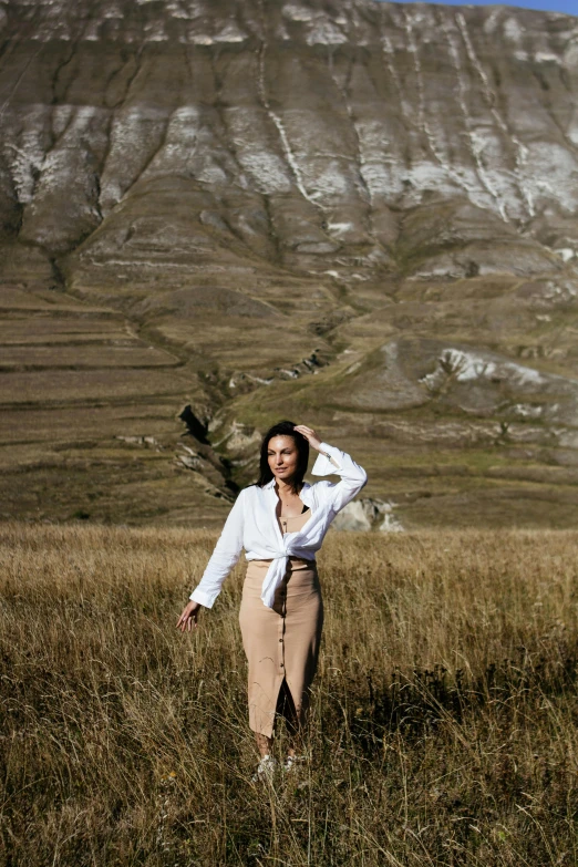 woman wearing a white shirt standing in field with mountain behind her