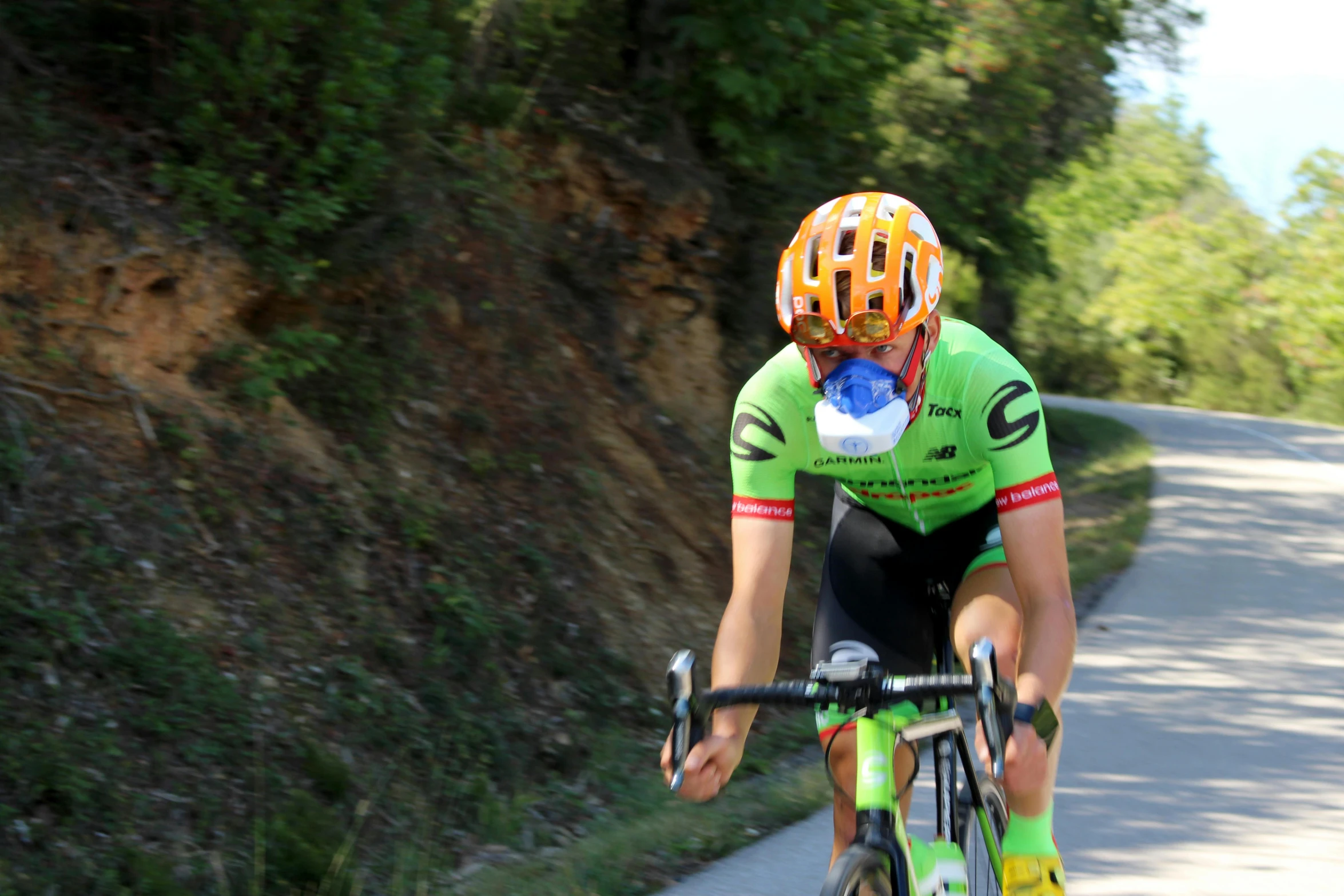 a cyclist riding on the street with trees and bushes