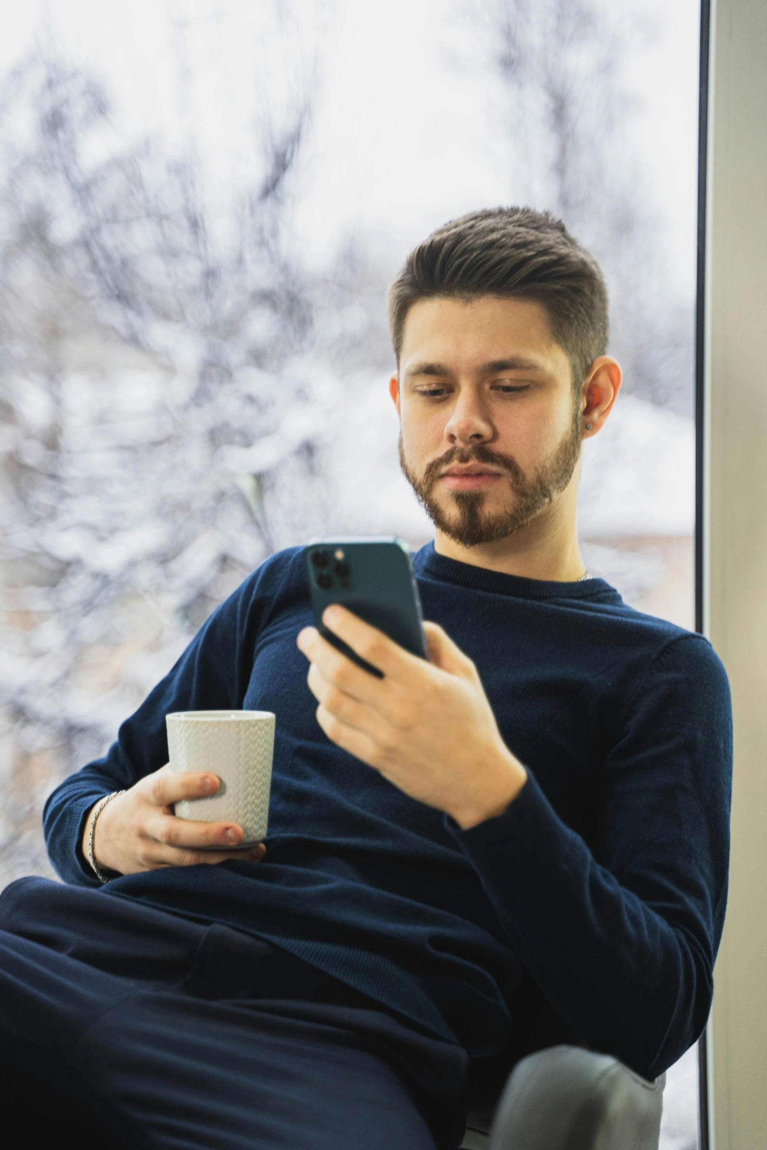 a man sitting in front of a window on his cell phone