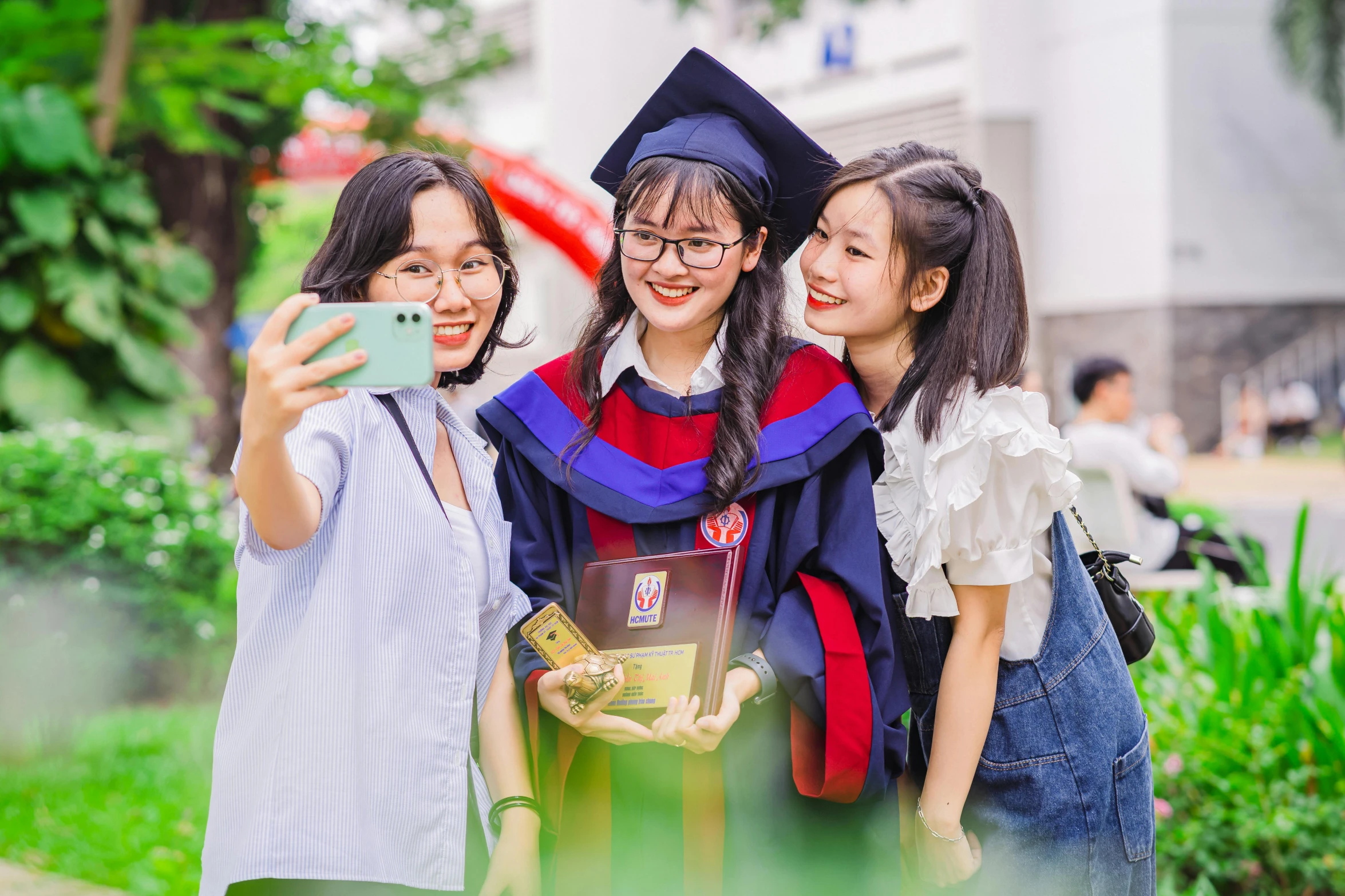 three girls in caps and gowns taking a selfie with their cell phone