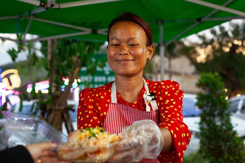 a woman in an apron holds food under a green awning