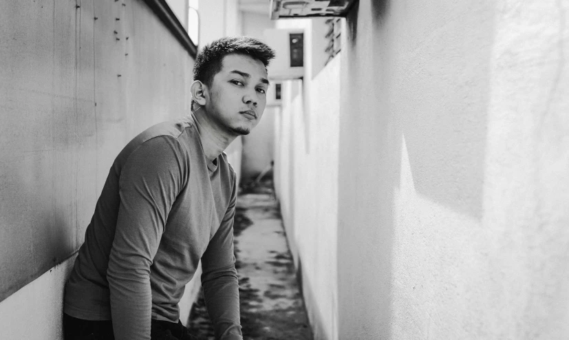 a young man leans against the wall in an alley way