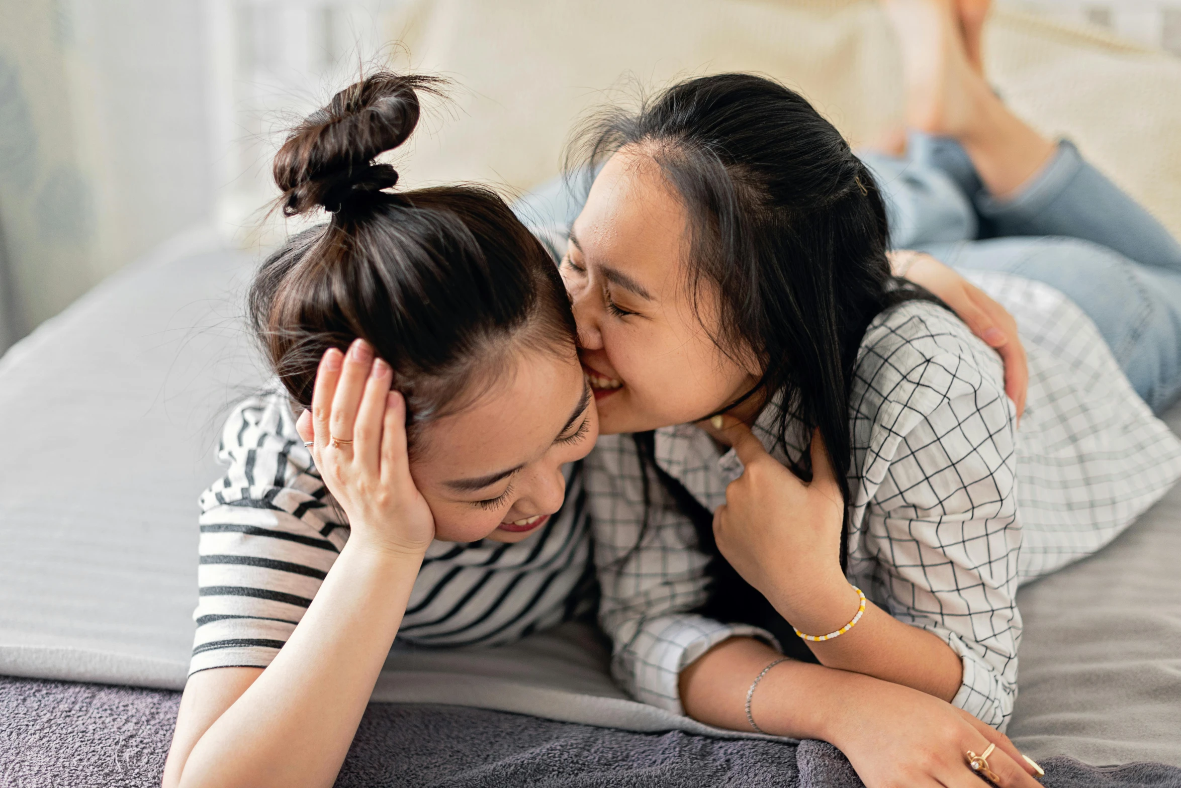 two young women laying on top of a bed with their arms around each other