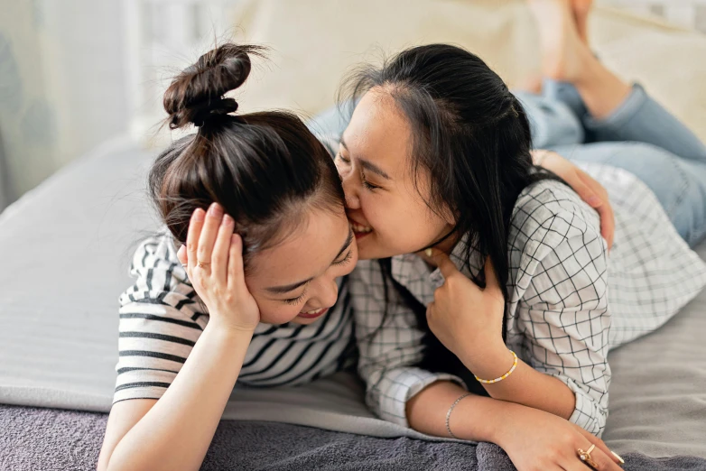 two young women laying on top of a bed with their arms around each other