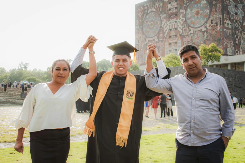 two couples in graduation attire with their arms in the air