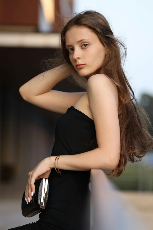 a woman with long hair sitting and holding a purse