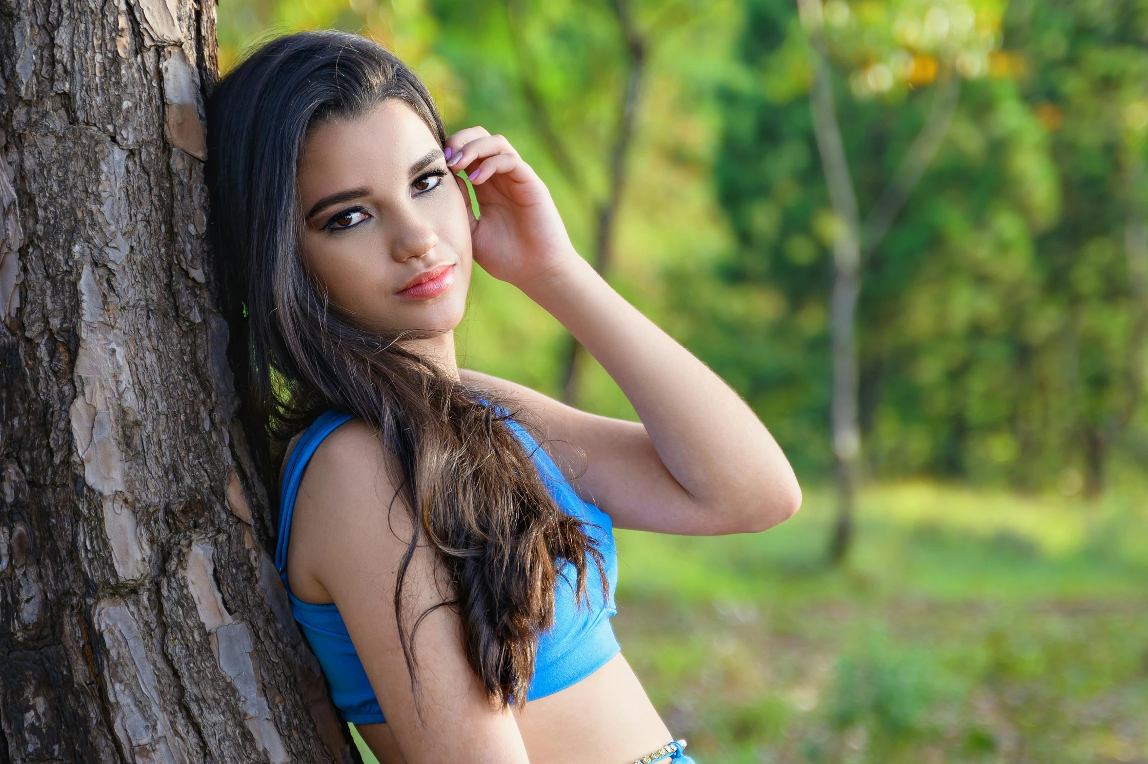 a woman is posing near a tree in a blue 