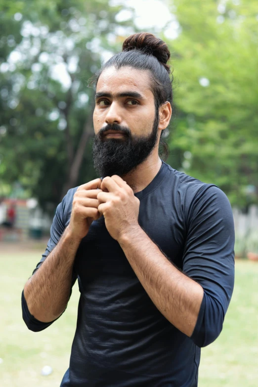 a man with a top knot standing with his hands clasped