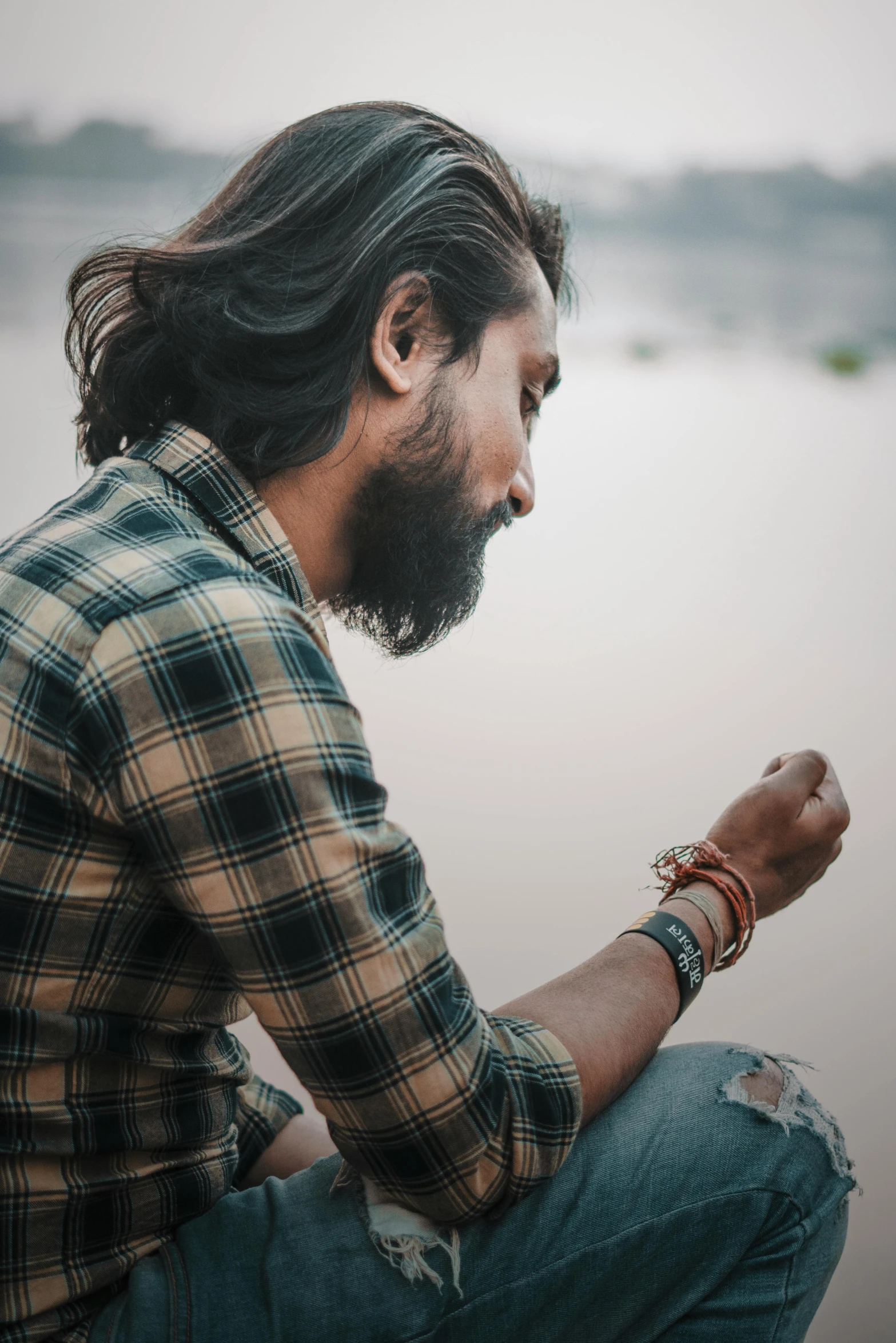 a man with long hair wearing celets sitting on the beach