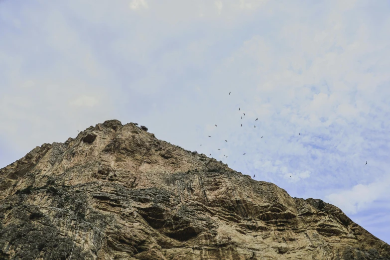 a bird flying through the sky near a rocky hill