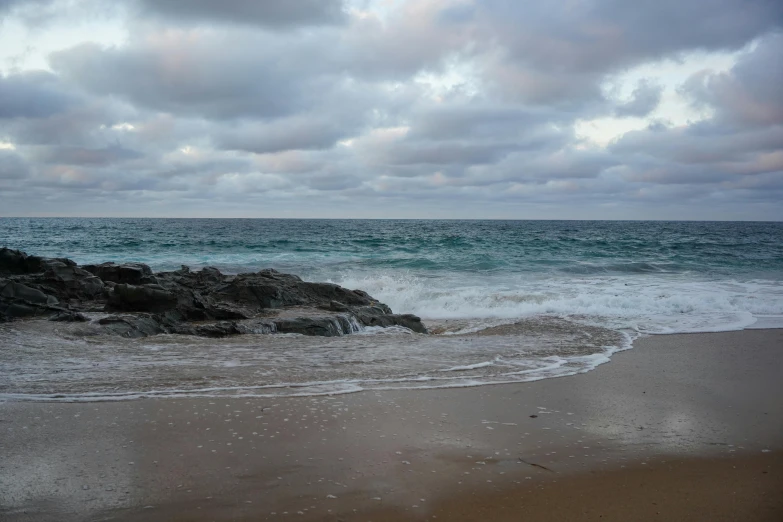 a rocky beach next to a small island with waves crashing