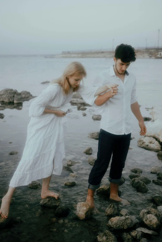 the man and woman are walking along the water