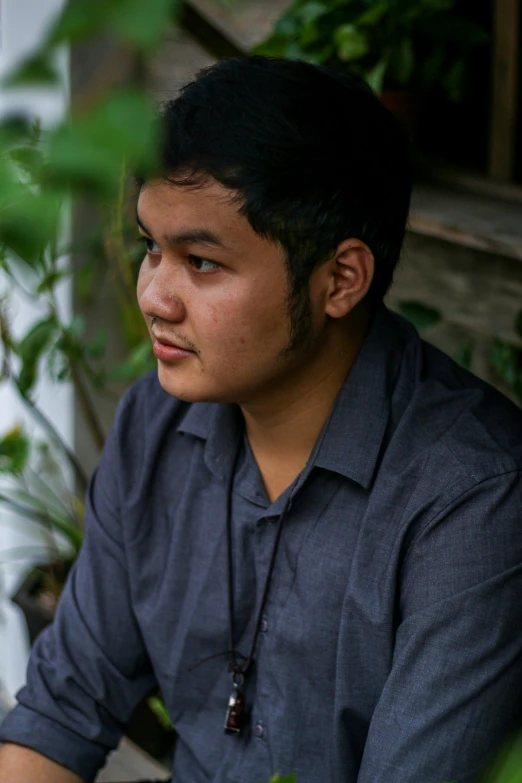 a man looking away from the camera wearing a necklace