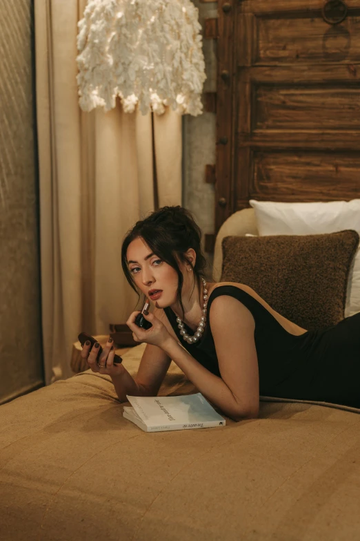 a woman in a black dress laying down on a bed talking on a phone
