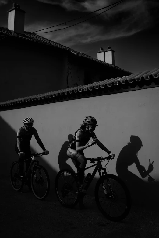 two cyclists wearing shorts and helmets are casting shadows in a black - and - white po