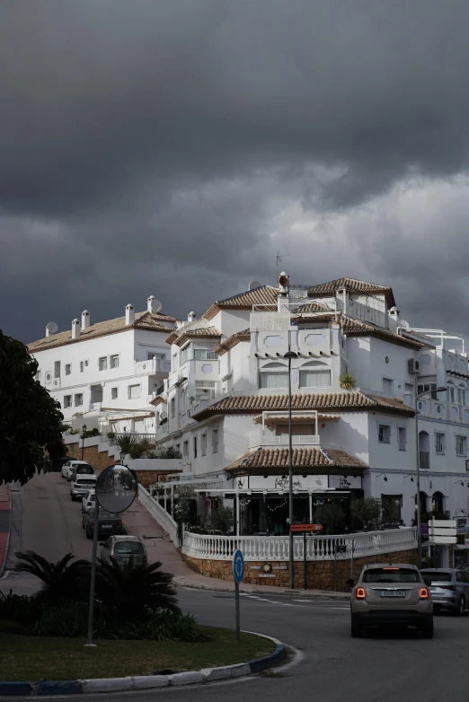 a road with many white buildings along the sides and dark clouds overhead