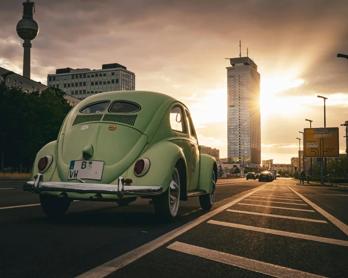 an antique car driving down a city street at sunset