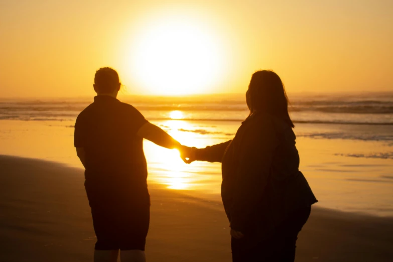 two people standing on a beach holding hands