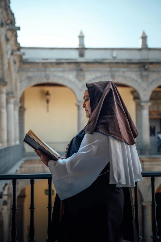 a woman in costume reads a bible while standing on the balcony