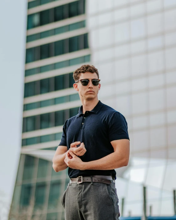 a young man stands in front of the building wearing sunglasses