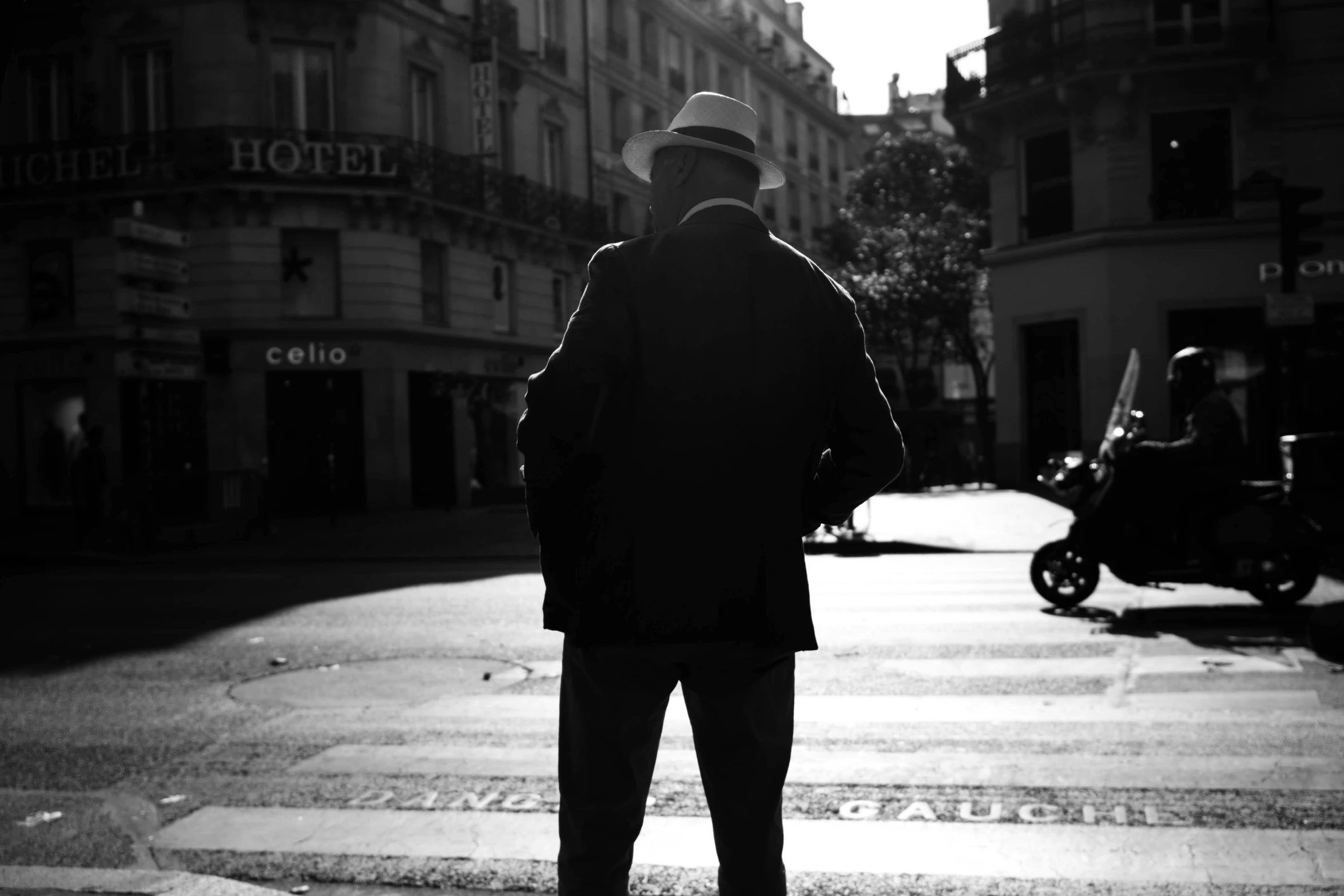 a man wearing a suit, hat and cane walks across an intersection