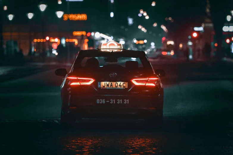 a dark city at night has the back lights of a car turning