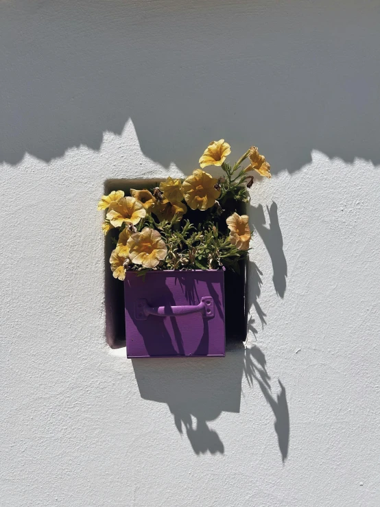 a purple vase with yellow flowers sits on a wall