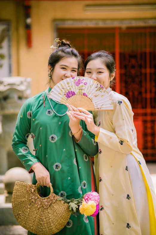 two women pose with one holding a fan and purse